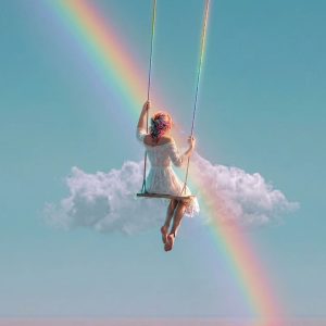 Woman in white dress on a swing suspended in the sky, reaching upward as a rainbow arcs through soft clouds over calm water.